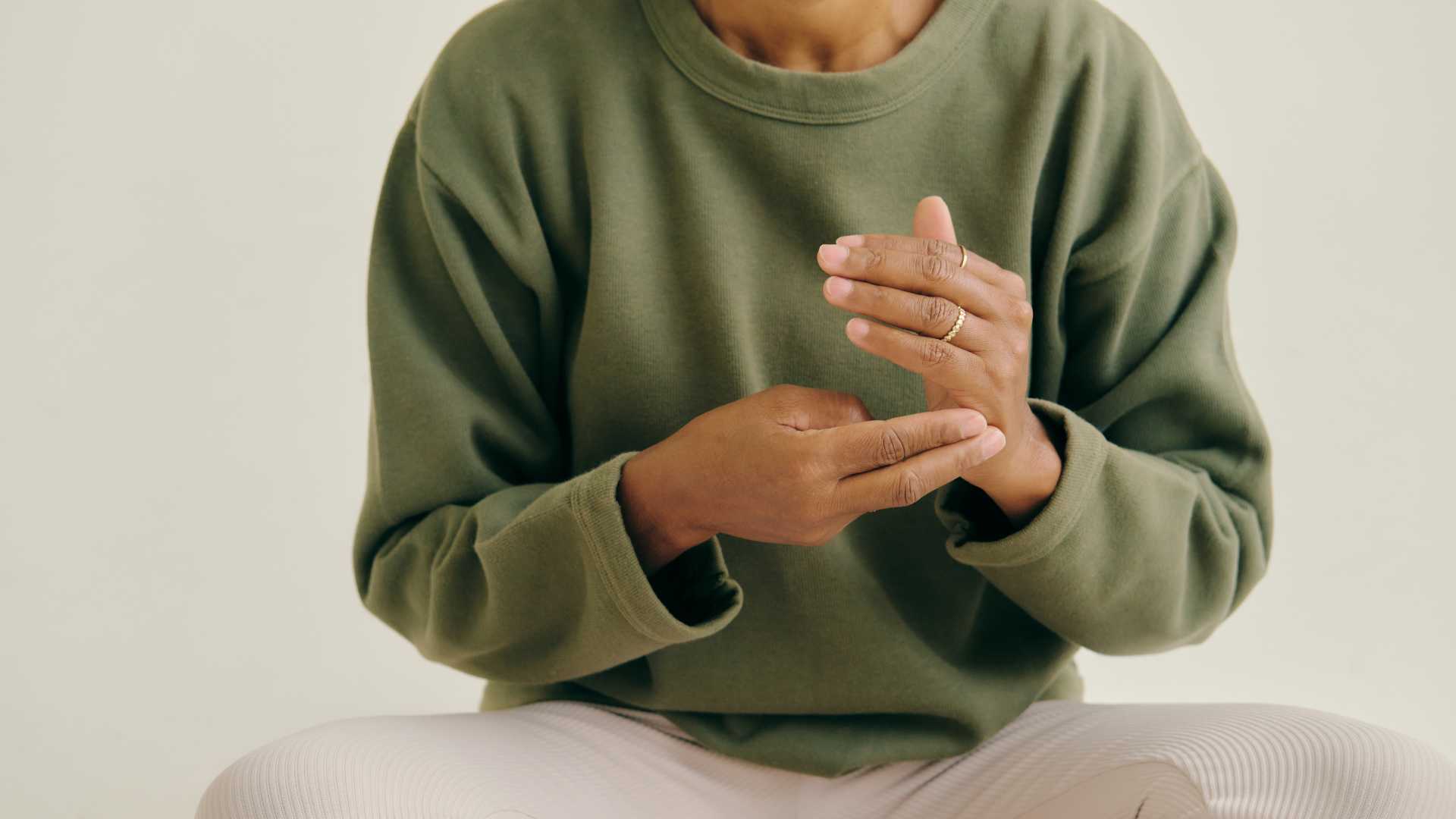 Femme qui médite avec un pull vert kaki et un pantalon blanc