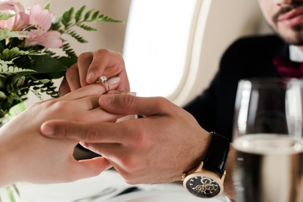 cropped view of man putting wedding ring on finger on woman while making marriage proposal in plane